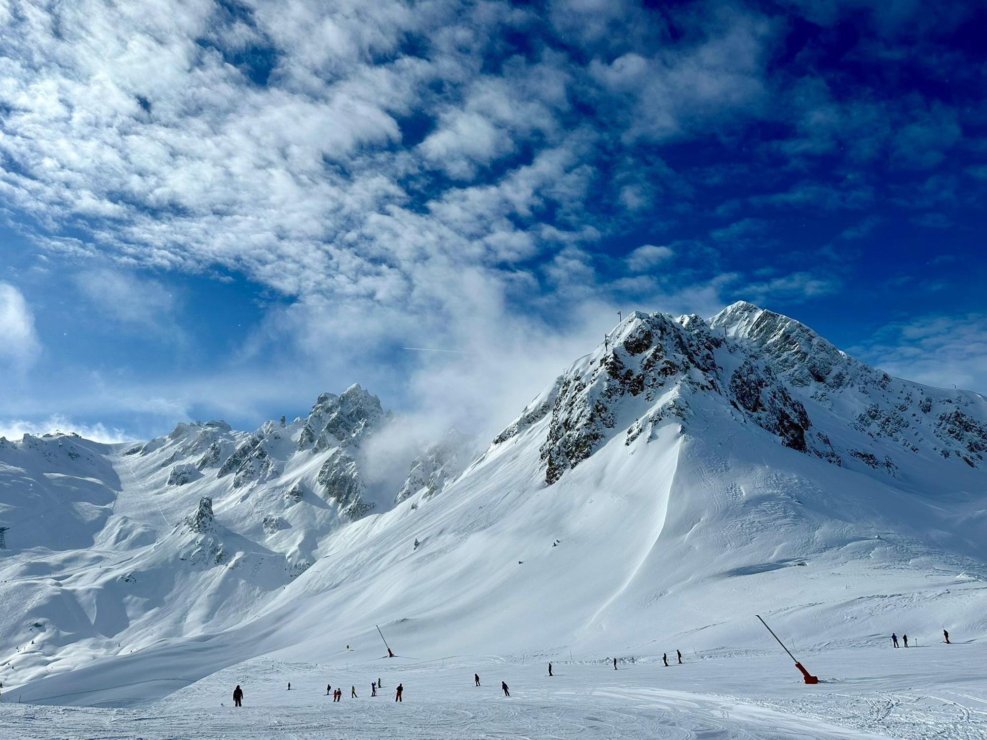 Esquiadores en una pista soleada bajo las cumbres nevadas de Courchevel